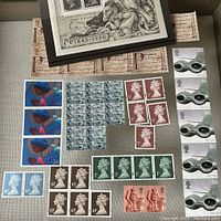 Top view of multiple British unused stamps including framed 1 pound 1840-1990 print, various 43p, 2p, 5p, 26p, 45p, 65p denomination stamps