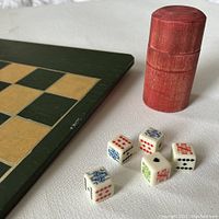 Close-up of game board corner, showing checkerboard pattern and six poker dice placed next to red wooden dice container.