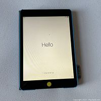 Apple iPad Mini powered on showing 'Hello' setup screen with blue edge and black front.