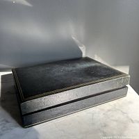 Closed jewelry box showing dark green leather with gold trim on edges.