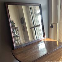 Mirror resting on a wooden surface with natural light reflection, showing frame and glass condition from a front angle