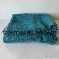 Folded teal mohair wool throw blanket showing fringe edges and texture.