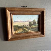 Framed miniature oil painting showing a rustic wooden frame and a scenic countryside landscape with a distant mountain range.