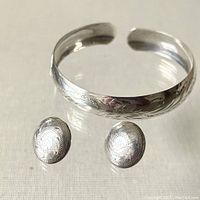 Set showing cuff bracelet and pair of round stud earrings together with etched designs.