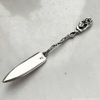 Full view of the silver cheese tool showing the blade and the entire handle with the garden nymph figure at the end.