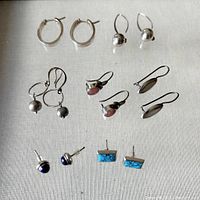 Overview of the seven pairs of sterling silver earrings showing various designs and colors including blue and turquoise stones, silver beads, and oval stones in drop and stud styles.