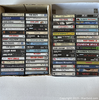 Photo showing multiple stacks of music cassette tapes with visible artist names and album titles from the 1970s and 1980s.