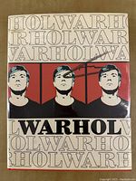 Front cover of dust jacket showing repeating 'WARHOL' text, triple portrait of Warhol, and black marker signature across the design.