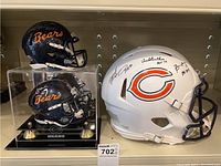 Two mini navy Chicago Bears helmets in acrylic display cases and one white full-size Chicago Bears helmet
