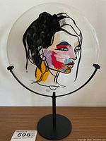 Front view of round glass disc with colorful abstract face painting on black metal stand