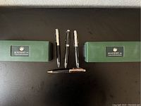Two closed Monteverde boxes flanking four pens on a black surface