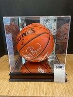 Full view of signed basketball inside clear acrylic display case on wood base