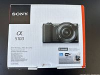 Front of sealed Sony α5100 box showing camera with 16-50mm kit lens and branding