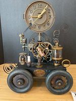Full front view of the steampunk clock sculpture on four wheels showing clock face, gears, springs and base