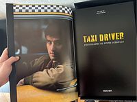Open book spread showing color photograph of Robert De Niro as Travis Bickle and title page reading 'Taxi Driver Photographs by Steve Schapiro'.