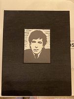 Black cloth slipcase top with mounted black-and-white block print portrait of Leonard Cohen