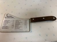 Photo of the entire metal menu card shaped like a cleaver with wooden handle on a retro patterned surface.