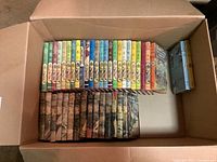 Box of vintage hardback books showing a full set of The Happy Hollisters books by Jerry West with colorful spines and illustrated scenes on jackets and a partial set of Kay Tracey mysteries by Frances K Judd with darker dust jackets.