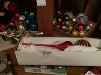 Photo of three boxes of assorted glass Christmas ball ornaments in multiple colors including red, blue, gold, green, and silver, and a white box containing a large red elongated glass tree topper with gold glitter decoration wrapped in white tissue paper.