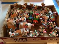 Photo of a box containing brass ornaments including teddy bears on Diet Coke cans, mice on Coke barrels, and a colorful toy train with a bear driver.