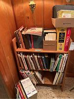 Photo of wooden small bookshelf filled with vintage and modern cookbooks, personal recipe binders, and boxes of recipe cards.