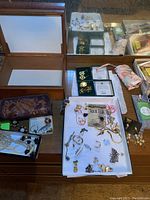 Overview of jewelry lot with multiple brooches, earrings, necklaces, and ring on table with some items in small boxes and a leather tooled item