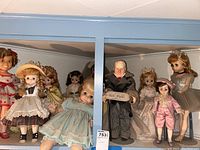 Front view of vintage 60s-70s dolls in blue shelf, showing variety including Shirley Temple and baby doll