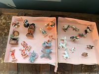 Two pink boxes on wooden surface containing assorted figurines laid out on paper