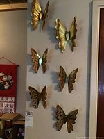 Six gold-tone metal butterfly wall art pieces mounted on a white wall, displaying their size and arrangement.