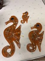 Three resin seahorse decorations on white star-patterned surface. Amber-orange color with embedded shiny flecks. All have black eyes and hooks on back visible.