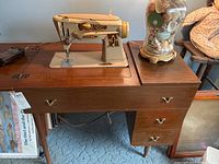 Singer vintage sewing machine installed in a wooden cabinet with three drawers with brass handles and a classic mid-century style.