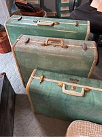 Three green vintage Samsonite suitcases stacked upright on a carpeted floor, showing cream trim and handles, close view