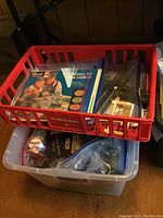 Red plastic crate and clear plastic bin containing assorted train cars, parts, and train catalogs.