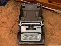 Overview of the Smith Corona Coronamatic electric typewriter sitting inside its hard plastic carrying case on brown carpet.