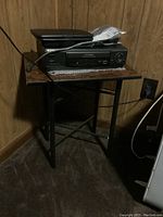 Sony VHS recorder model SLV-2090 and RCA portable DVD player placed on a small table in corner of room, cords visible.