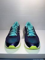 Front view of navy blue ladies running shoes with teal laces and lime green accents on the sole and toe area.