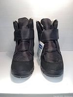 Front view of the black unisex boots showing the adjustable strap and tag intact.