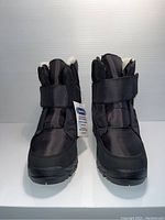 Front view of brand new pair of black unisex boots with Velcro closure and visible white fleece lining inside.