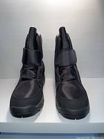 Front view of black unisex boots, showing Velcro strap closure and nylon upper material.