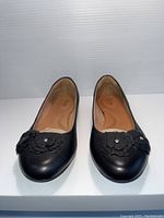 Front view of new black leather Clarks flats showing decorative flower appliques on toes.