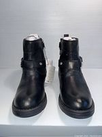 Front view of pair of black leather kids boots showing smooth toe and buckle strap on ankle.