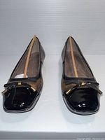 Front view of pair of ladies shoes showing the black patent square toes and decorative bows.
