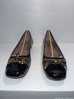 Front view of a pair of brown and black patterned flats with black patent leather toe caps and bow detail