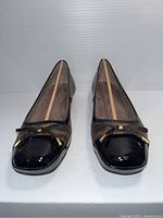 Front view of the pair of ladies shoes showing black patent toe cap, bow with gold tips, brown and black patterned upper.