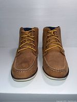 Front view of pair of brown Sperry kids boots showing moc-toe stitching and yellow laces.