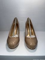 Front view of pair of nude patent leather high heel pumps with pointed toe, showing both shoes upright and symmetrically positioned.