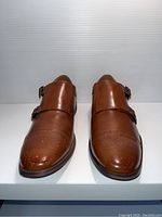 Front view of the pair of men's brown leather monk strap shoes showing brogue detailing and buckle straps.
