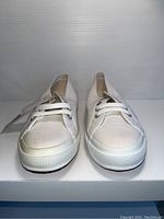 Front view of a pair of off-white Superga canvas shoes with white laces and white rubber sole.