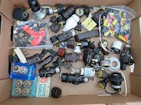Top view of large box containing various electrical parts including plastic bags of wire connectors, multiple plugs and sockets, packaged fuses, and lamp switch ends.