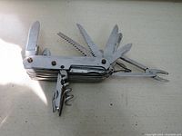 Metal multi-tool pocket knife unfolded showing multiple tools like saw blades, knives, pliers and corkscrew